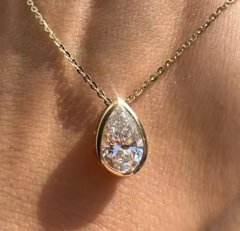Gold necklace with a teardrop-shaped diamond pendant on a hand.